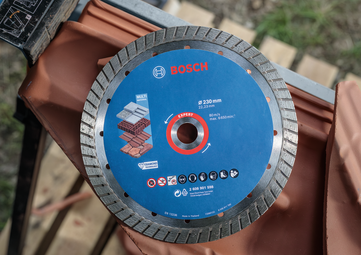 Bosch EXPERT MultiMaterial Diamond Cutting Disc 230mm placed on tile surface showing multi-material cutting icons.