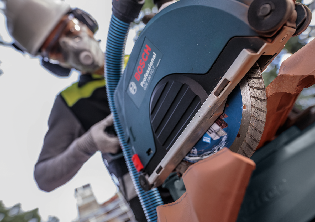 Worker operating Bosch EXPERT MultiMaterial Diamond Cutting Disc 230mm on tile with protective gear and grinder.