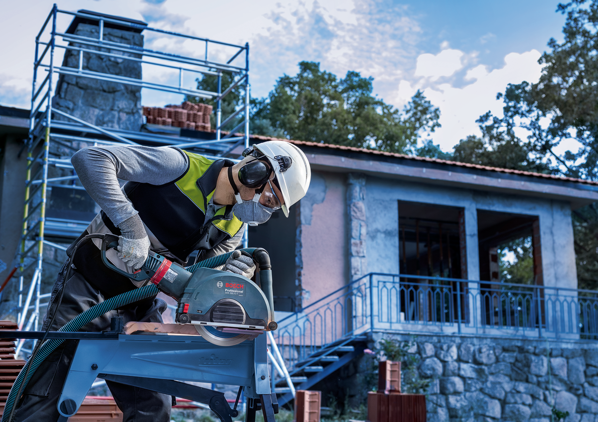 Construction worker cutting tile with Bosch EXPERT MultiMaterial Diamond Cutting Disc 230mm outdoors near a house.
