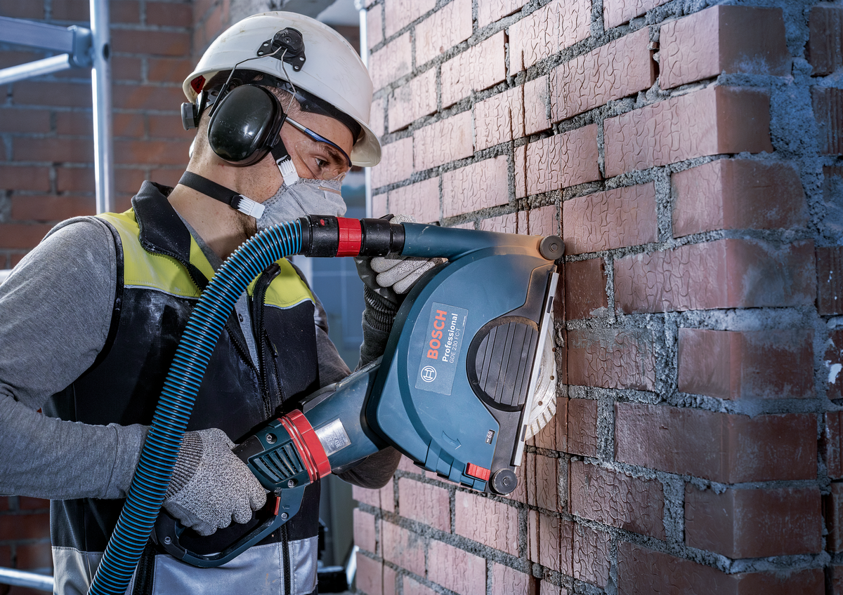Worker using Bosch EXPERT MultiMaterial Diamond Cutting Disc 230mm to cut brick wall with dust extraction system.