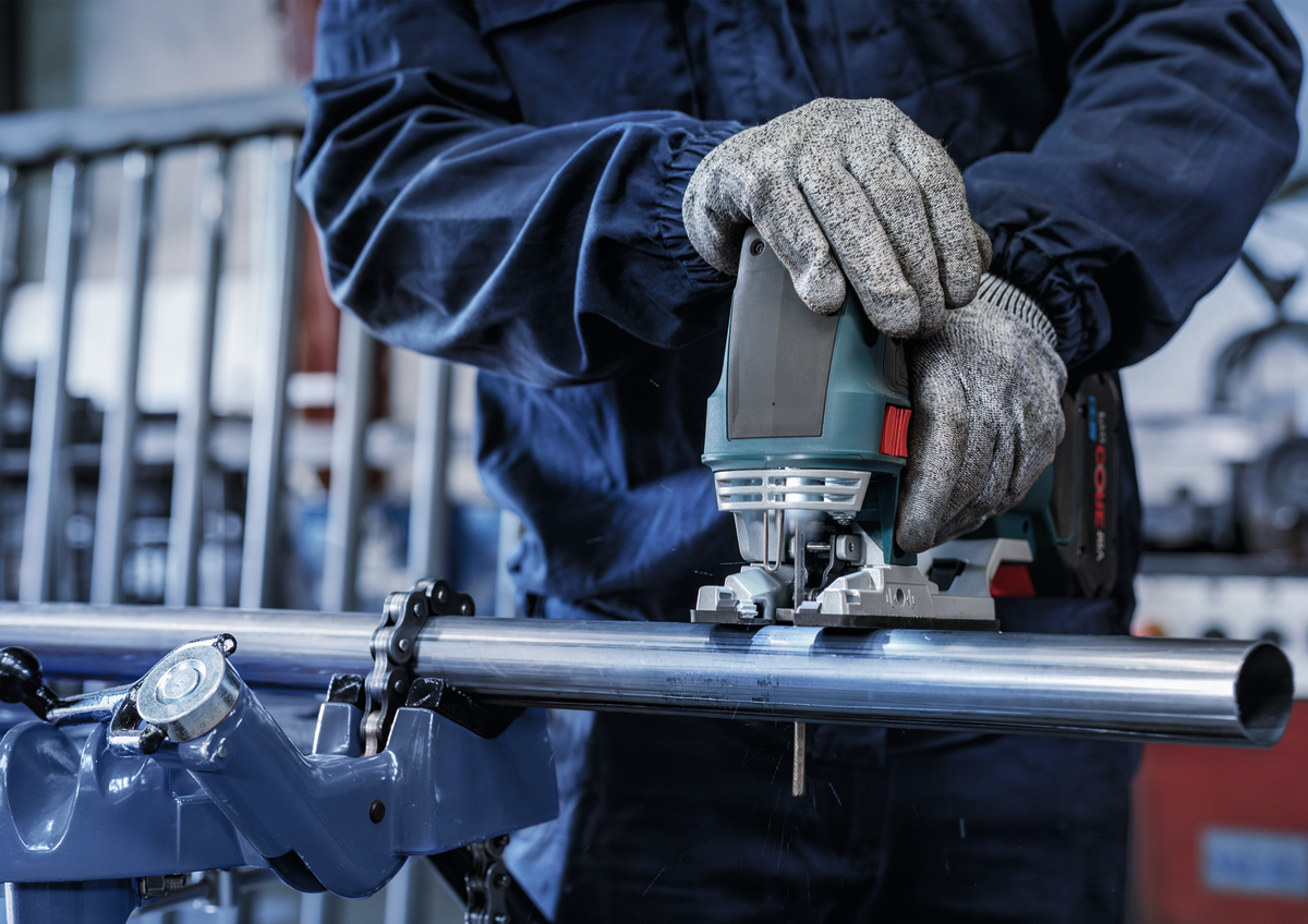 Worker using Bosch jigsaw and T321BF blade to cut a metal pipe, showcasing tool control and blade precision in metalwork.