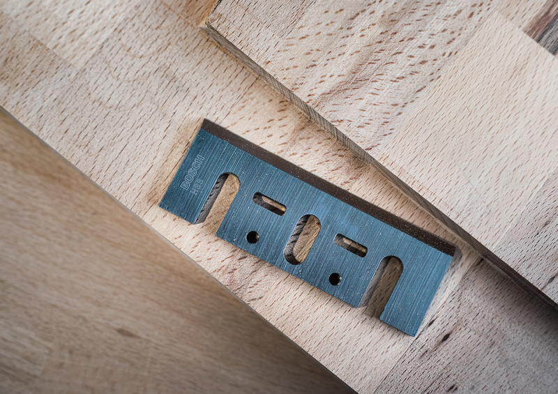 Angled view of Bosch PRO Planer Knife, 82 x 29 x 3 mm 2608635905 on wood, showcasing its cutting edge and robust construction for planers.