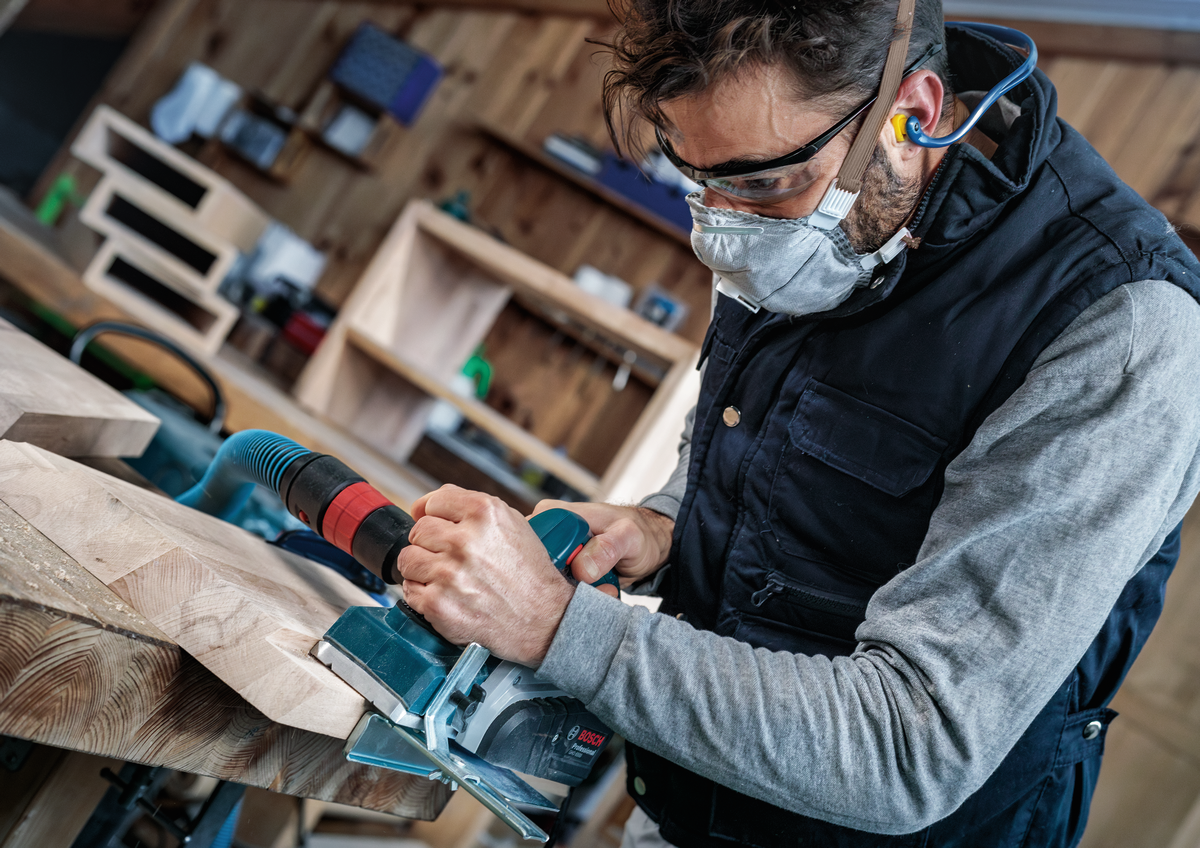 Woodworker using Bosch PRO Planer Knife, 82 x 29 x 3 mm 2608635905 in workshop, wearing safety gear while planing a wooden board.