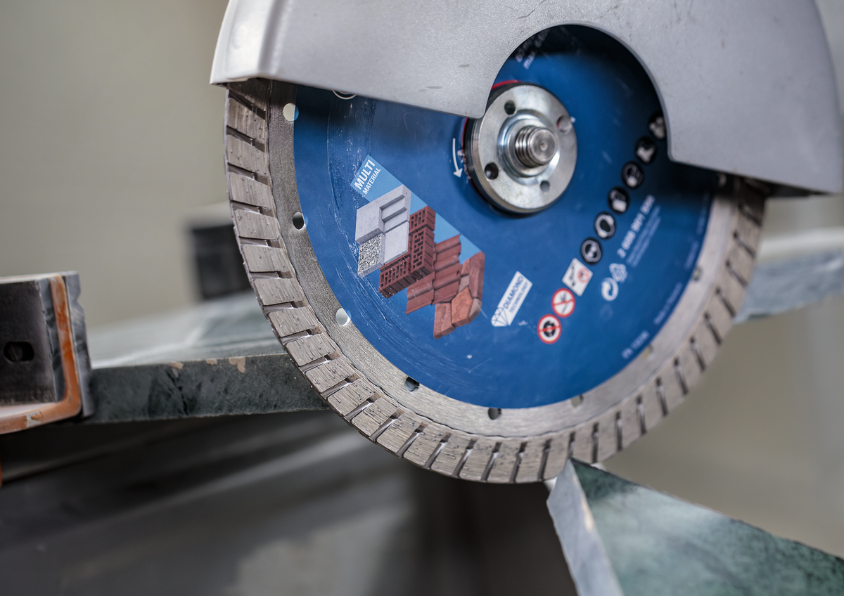 Bosch EXPERT MultiMaterial Diamond Cutting Disc 230mm cutting through metal with precision on a workbench.