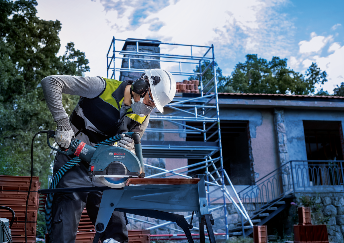 Bosch EXPERT MultiMaterial Diamond Cutting Disc 230mm cutting tile on a construction site with scaffolding in background.