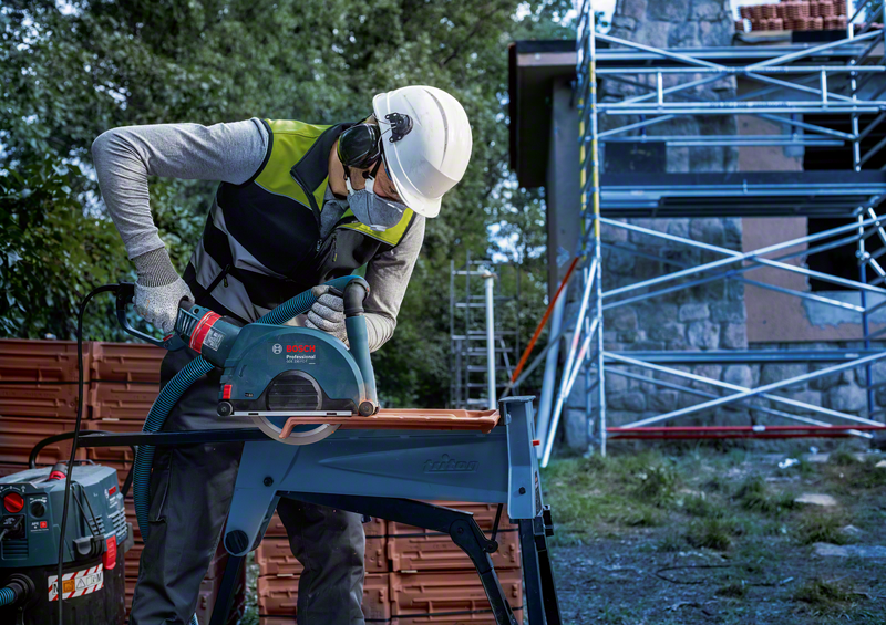 Professional using Bosch EXPERT MultiMaterial Diamond Cutting Disc 230mm to cut building material on a stand outdoors.
