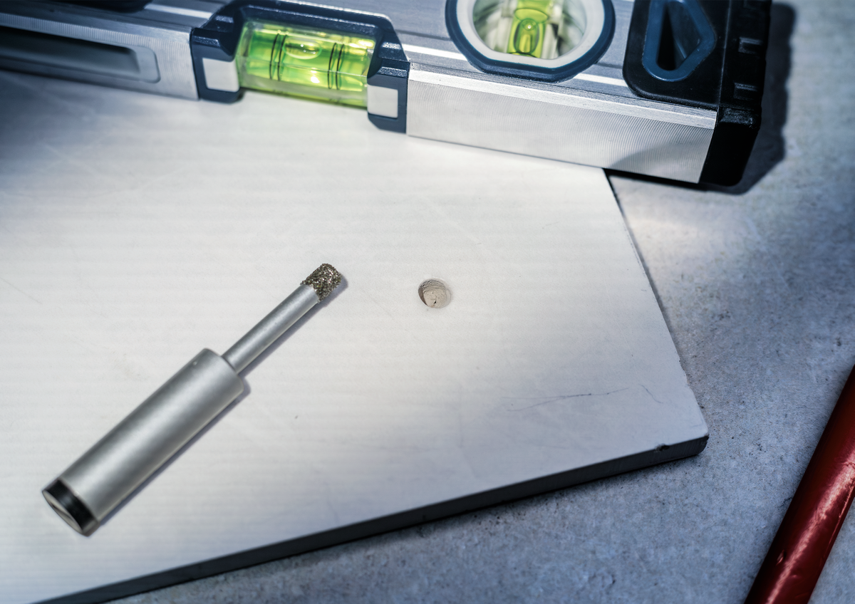 Bosch PRO Ceramic dry Drill Bit next to drilled hole in tile, showing clean cut and accuracy for ceramic and porcelain applications.