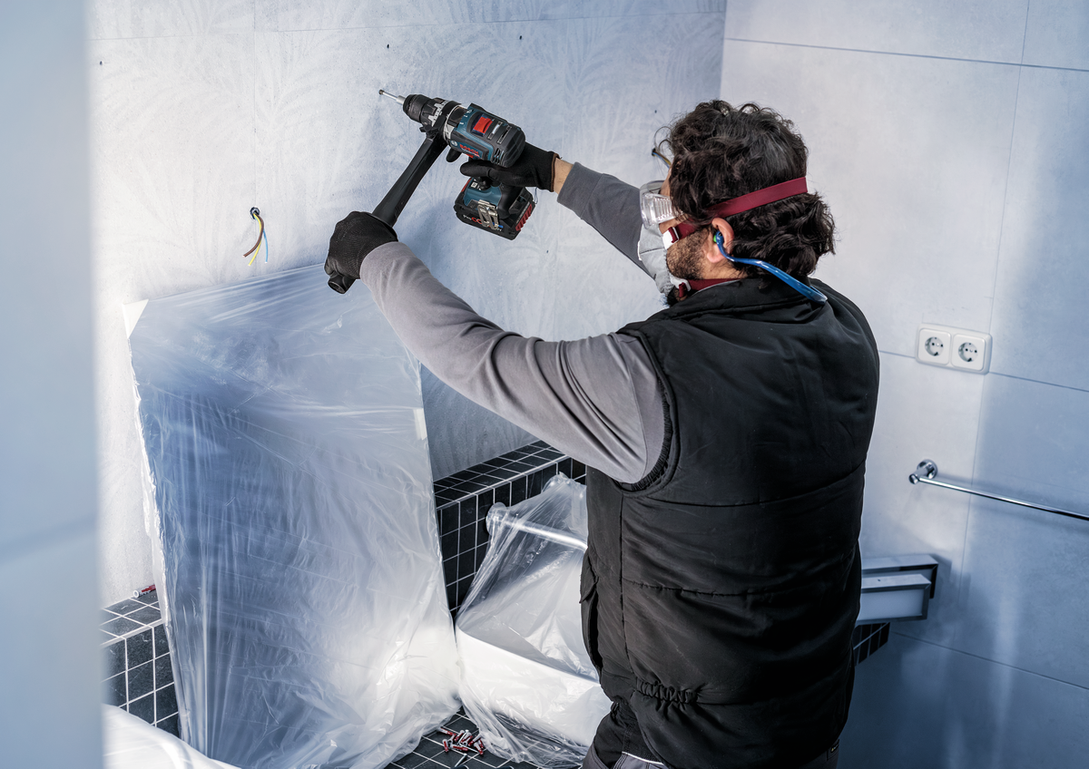 Professional using Bosch PRO Ceramic dry Drill Bit with cordless drill on bathroom wall tiles, showcasing tool in real-life application.