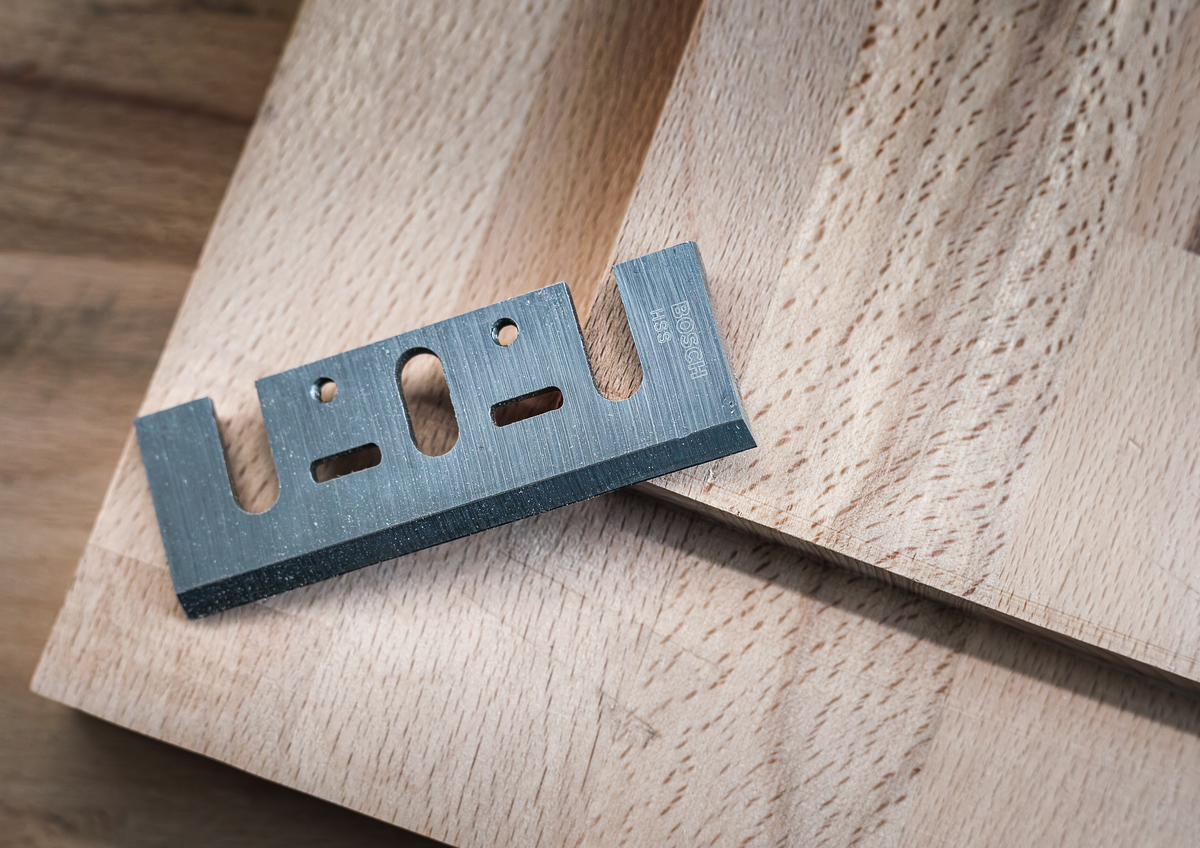 Bosch PRO Planer Knife, 82 x 29 x 3 mm 2608635905 placed on wooden surface, highlighting its sharp edge and durable build for woodworking tasks.